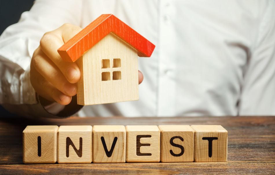 Wooden blocks with the word Invest and house in the hands of a businessman. The concept of investing in real estate construction. Effective investment. Buying apartments. Business and finance Wooden blocks with the word Invest and house in the hands of a businessman. The concept of investing in real estate construction. Effective investment. Buying apartments. Business and finance
