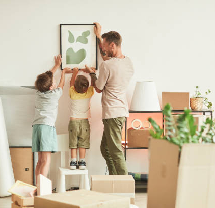 istockphoto-1349049467-612×612 Full length portrait of happy father with two sons hanging pictures on wall while moving in to new home, copy space